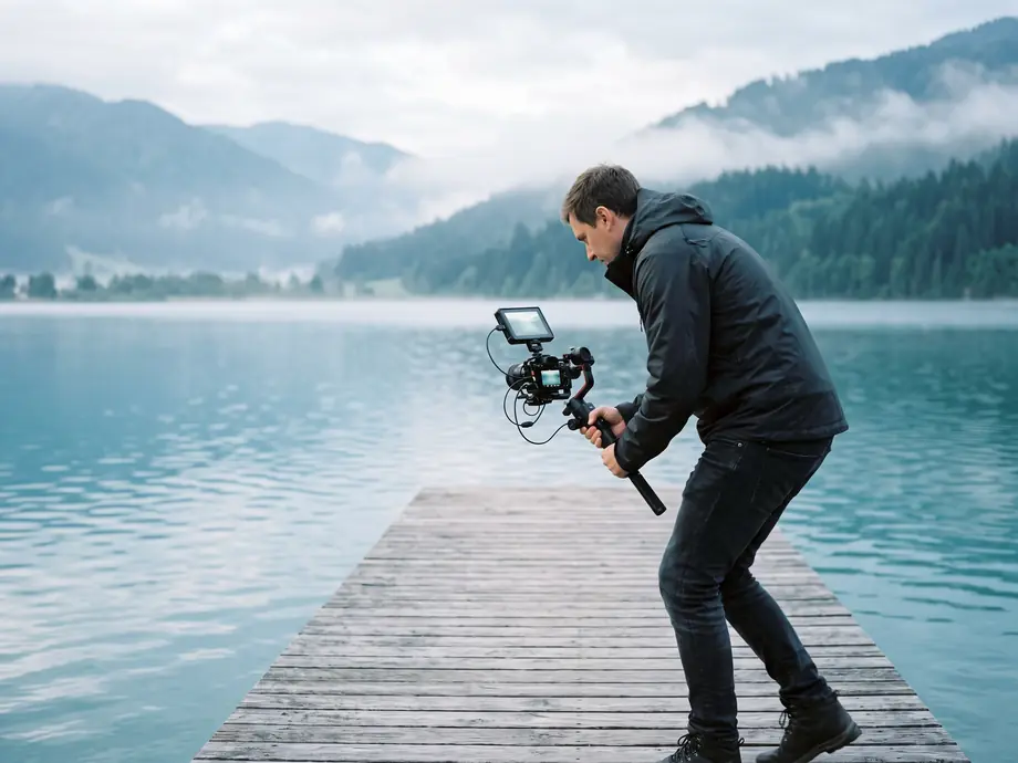 Videograf mit Gimbal-Kamera auf einem Steg am See
