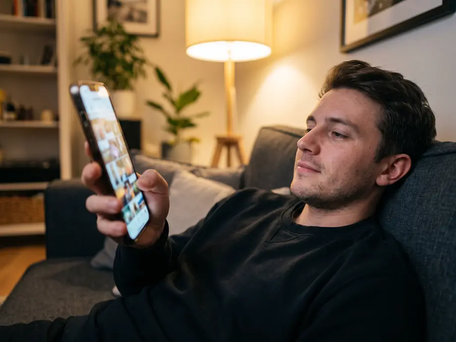 Mann scrollt abends auf dem Sofa durch Fotos am Smartphone