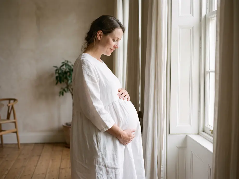 Schwangere Frau im weißen Kleid am Fenster